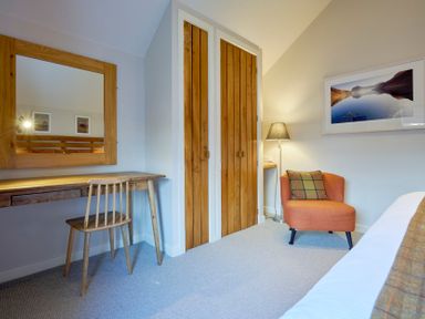 A bedroom with a wooden desk and chair a mirror wooden closet doors an orange chair with a plaid cushion a floor lamp and a framed picture on the wall at Howe Keld 5 First Floor in Keswick
