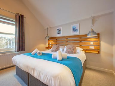A bedroom with a double bed with a blue runner and rolled towels at Howe Keld 5 First Floor in Keswick