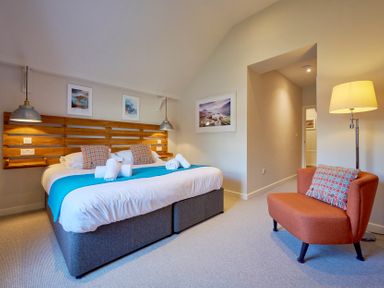 A bedroom with a double bed with folded towels and pillows an orange chair with a patterned cushion and a floor lamp at Howe Keld 5 First Floor in Keswick