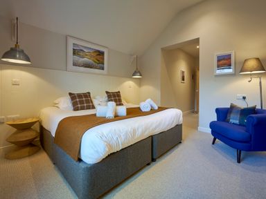 A bedroom with a large bed two brown pillows a blue armchair and a floor lamp at Howe Keld 5 First Floor in Keswick