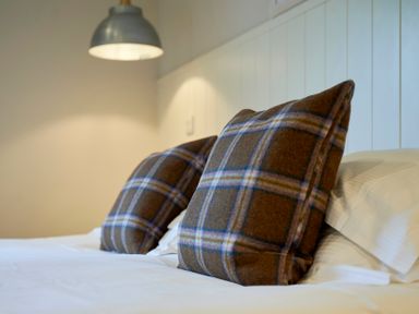 Two plaid pillows on a bed with white sheets and a wall lamp above the headboard at Howe Keld 5 First Floor in Keswick