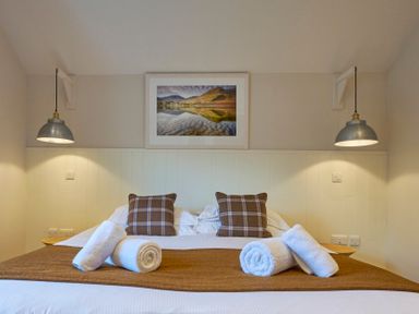 A bedroom with a double bed two plaid pillows rolled white towels hanging lamps and a landscape picture on the wall at Howe Keld 5 First Floor in Keswick