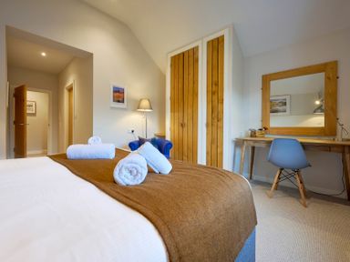 A bedroom with a bed with towels on it a blue chair a wooden wardrobe and a wooden desk with a blue chair Howe Keld 5 First Floor in Keswick
