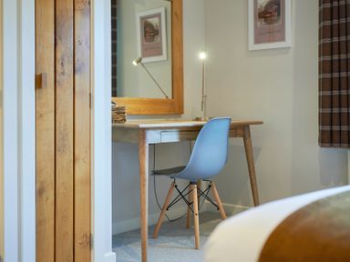A small wooden desk with a modern chair and a lit desk lamp in a room at Howe Keld 5 First Floor in Keswick
