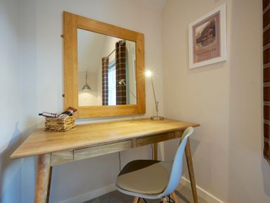 A small wooden desk with a basket and a lamp a white chair and a large wooden framed mirror on the wall at Howe Keld 5 First Floor in Keswick