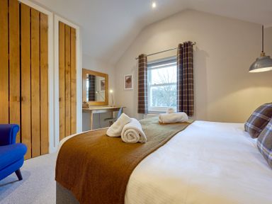 A bedroom with a bed with folded towels a wooden desk and mirror a blue chair and wooden closet doors at Howe Keld 5 First Floor in Keswick