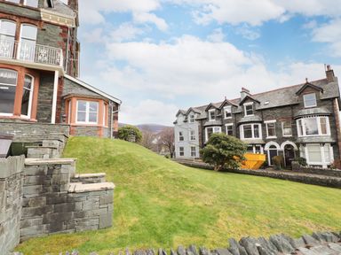A grassy slope with stone steps leading up to houses with stone and brick exteriors at Howe Keld 6 Second Floor in Keswick