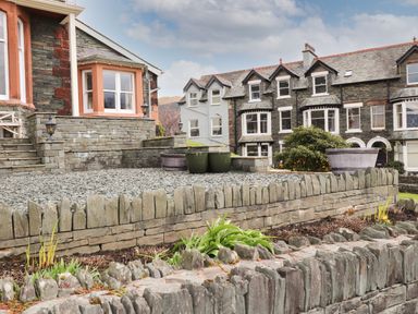 A stone patio area with planters and a tiered stone wall in front of residential buildings at Howe Keld 6 Second Floor in Keswick
