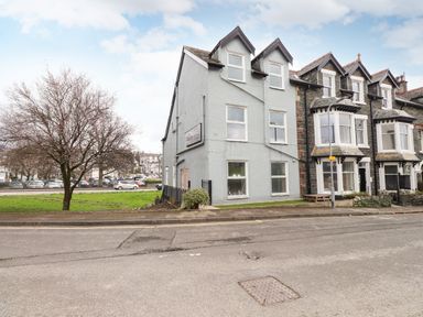 A street view showing a row of houses with a grassy area and parked cars nearby at Howe Keld 6 Second Floor in Keswick
