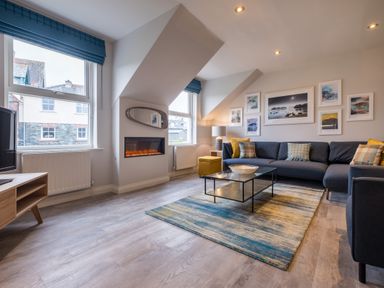 A living room with a sectional sofa, glass coffee table, electric fireplace, and wall art at Howe Keld 6 Second Floor in Keswick