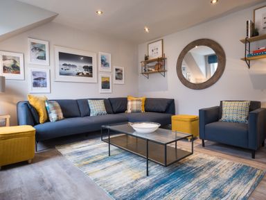 A living room with a blue sofa and armchair a glass coffee table and yellow ottomans at Howe Keld 6 Second Floor in Keswick