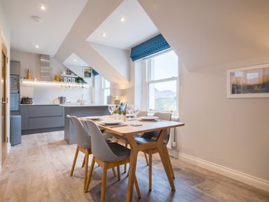 A kitchen and dining area with a wooden table set with plates and glasses and a grey cabinetry kitchen in the background at Howe Keld 6 Second Floor in Keswick