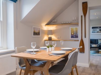 A dining area with a wooden table set for four with plates and glasses and gray chairs at Howe Keld 6 Second Floor in Keswick
