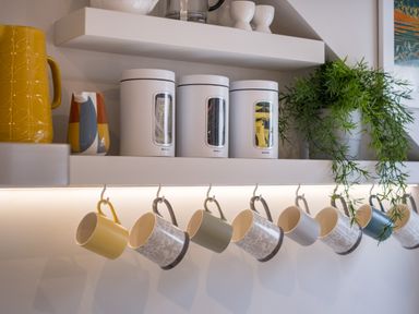 A kitchen shelf with white canisters yellow pitcher multicolored jug green plant and mugs hanging below at Howe Keld 6 Second Floor Keswick