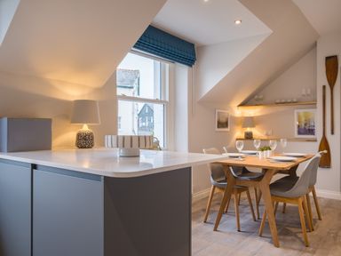 A dining area with a wooden table set for four and a kitchen island with a lamp and decorative bowl at Howe Keld 6 Second Floor in Keswick