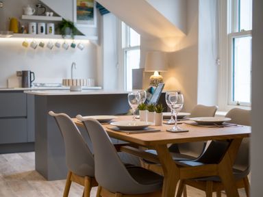 A dining area with a wooden table set with plates and wine glasses next to a modern kitchen at Howe Keld 6 Second Floor in Keswick