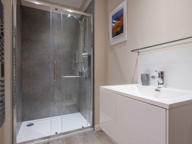 A shower area with glass doors and a sink with a faucet and framed picture in a bathroom at Howe Keld 6 Second Floor in Keswick
