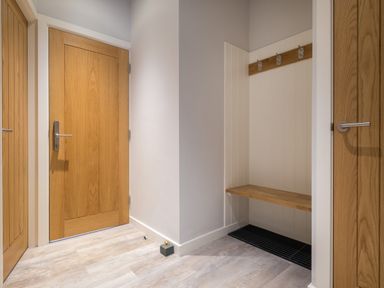 A hallway with wooden doors a built-in wooden bench with hooks and a black floor mat at Howe Keld 6 Second Floor in Keswick
