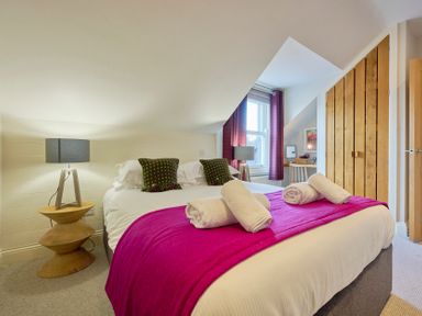 A bedroom with a double bed rolled towels bedside lamps wooden wardrobe and a window with curtains at Howe Keld 6 Second Floor in Keswick