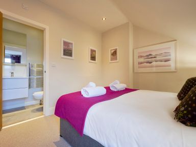 A bedroom with a bed, white towels on a purple runner, and framed pictures on the walls at Howe Keld 6 Second Floor in Keswick
