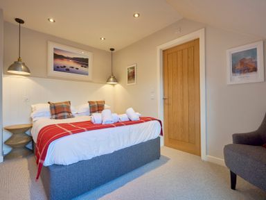 A bedroom with a double bed pillows and rolled towels with a wooden door and armchair at Howe Keld 6 Second Floor in Keswick