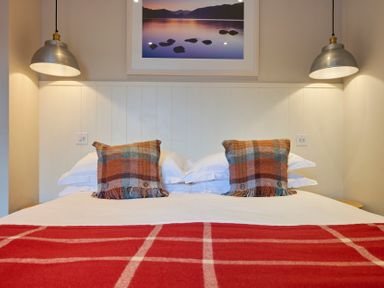 A bed with two plaid pillows and a red blanket with white lines under two hanging lights and a framed photo on the wall at Howe Keld 6 Second Floor in Keswick
