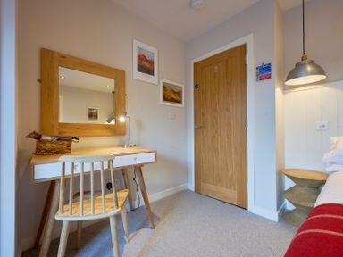 A bedroom corner with a wooden desk and chair a mirror two framed pictures a wooden door and a bedside table with a pendant light at Howe Keld 6 Second Floor Keswick