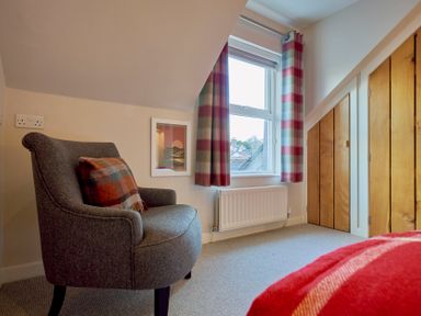 A bedroom corner with a gray armchair and plaid cushion a window with plaid curtains radiator and wooden closet doors at Howe Keld 6 Second Floor Keswick