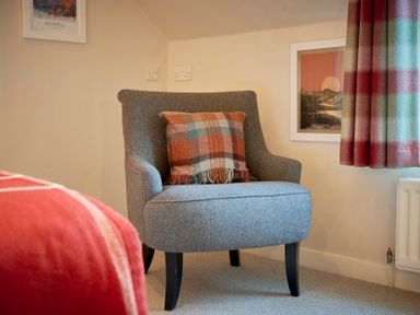 A gray upholstered chair with a checkered cushion next to a window with checkered curtains and framed pictures on the walls at Howe Keld 6 Second Floor in Keswick