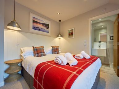 A bedroom with a double bed featuring plaid pillows and a red blanket with rolled towels by the bedside tables Howe Keld 6 Second Floor Keswick