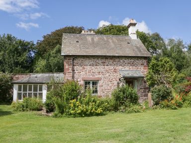 A stone cottage with a garden and flowers in front at Caldhu Cottage in Holmrook
