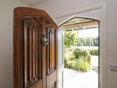 A wooden door partially open showing a garden with bushes and trees outside at Caldhu Cottage in Holmrook
