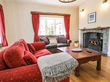 A living room with red and brown sofas a wooden coffee table and a fireplace at Caldhu Cottage in Holmrook