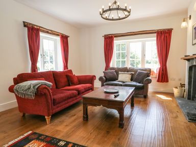 A living room with red and brown sofas a wooden coffee table wooden floor and windows with red curtains at Caldhu Cottage in Holmrook