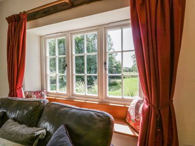 A window with white frames red curtains and cushions on a wooden bench behind a dark sofa at Caldhu Cottage in Holmrook