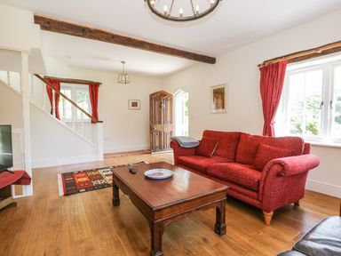 A living room with a red sofa wooden coffee table patterned rug and wooden front door at Caldhu Cottage in Holmrook