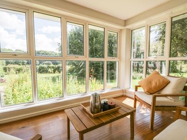A sunroom with wooden chairs and a table with a tray and a thermos outside garden windows at Caldhu Cottage in Holmrook