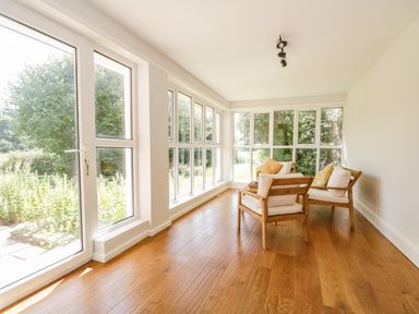 A sunroom with wooden floor and two armchairs with cushions near large windows at Caldhu Cottage in Holmrook