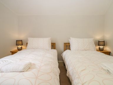 A bedroom with two single beds bedside tables and lamps at Caldhu Cottage in Holmrook