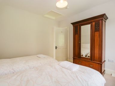 A bedroom with two beds a wooden wardrobe with mirror and a white door at Caldhu Cottage in Holmrook