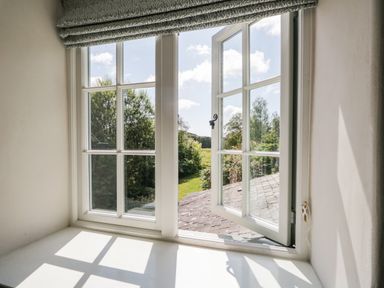 Window with an open pane and roman blind showing trees and greenery outside at Caldhu Cottage in Holmrook