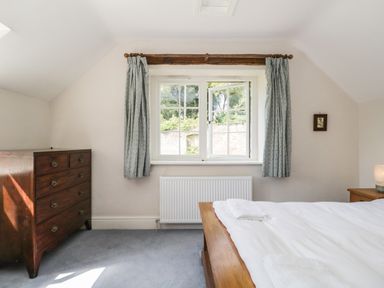 A bedroom with a wooden bed white bed linen a wooden chest of drawers and a window with curtains at Caldhu Cottage in Holmrook