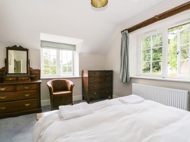 A bedroom with a bed, wooden dresser with mirror, chest of drawers, leather chair and two windows at Caldhu Cottage in Holmrook