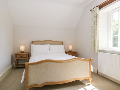 A bedroom with a wooden bed a window with curtains and two bedside tables with lamps at Caldhu Cottage in Holmrook