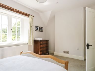 A bedroom with a wooden bed frame a wooden chest of drawers with folded towels on top two framed pictures on the wall and a window with curtains at Caldhu Cottage in Holmrook