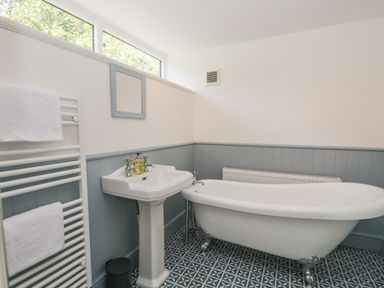 A bathroom with a clawfoot bathtub a pedestal sink with soap a towel rack with towels and patterned floor tiles at Caldhu Cottage in Holmrook