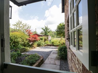 A garden with a gravel path and plants viewed from an open door at Caldhu Cottage in Holmrook