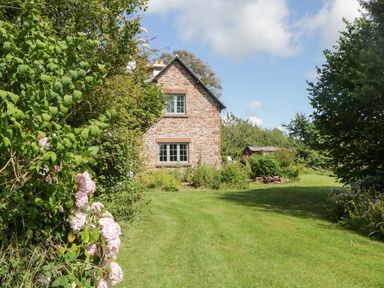 A stone cottage with windows surrounded by grass lawn and trees at Caldhu Cottage in Holmrook