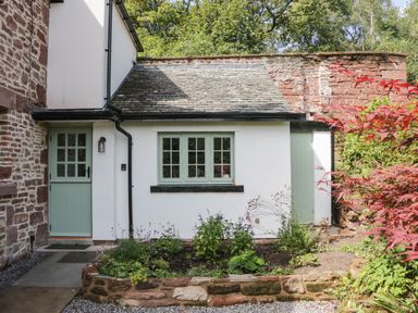 Exterior view of a cottage with a stone wall, green door and windows and a small garden bed in front of Caldhu Cottage in Holmrook