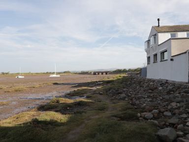 A coastal scene with boats on mudflats a rocky shoreline and a white building at Caldhu Cottage in Holmrook
